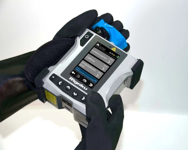 image of gloved hands holding a Rigaku ResQ CQL model handheld Raman spectrometer, with the screen displaying possible mixtures to analyze