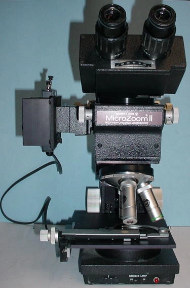 Bausch and Lomb MicroZoom II long working distance microscope mounted on R stand. 10x eyepieces and 2.25, 8 and 25 power objectives. Secondary focusing block can be removed to center objectives over the stage. Reflected light only 115 volts 50/60 28#